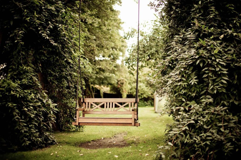 10 easy garden ideas. This is an image of a garden housing a lot of giant shrubbery and a swing centered in the middle of the photo within the garden.