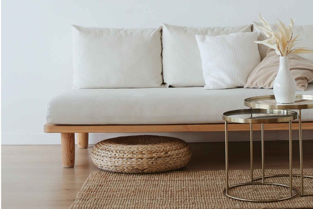 How to make your home look like you hired an interior designer. This is an image of a modern boho styled livingroom setup. There is an offwhite couch and a coffee table with a floor pillow peeking out from under the couch.