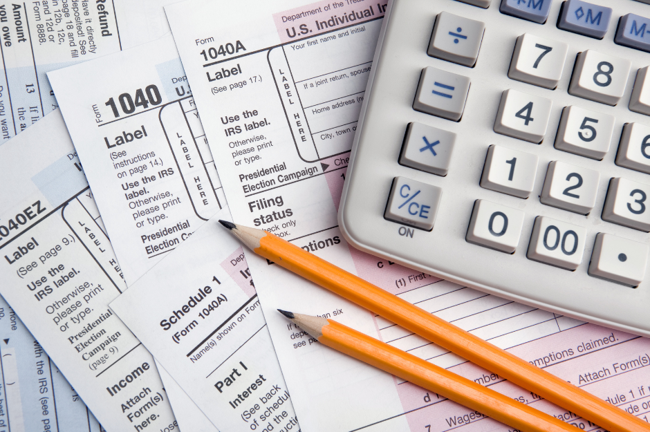 Tax documents spread out on table with two pencils and a calculator on top of them.